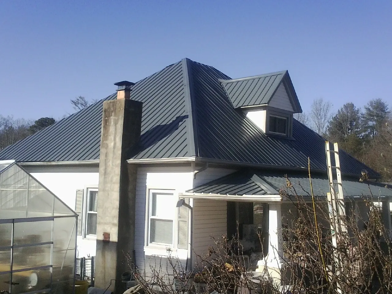 Dark blue standing seam metal roof on a white farmhouse with dormer — Slate & Tile Roof Repair by Roofing Brothers in Martinsdale
