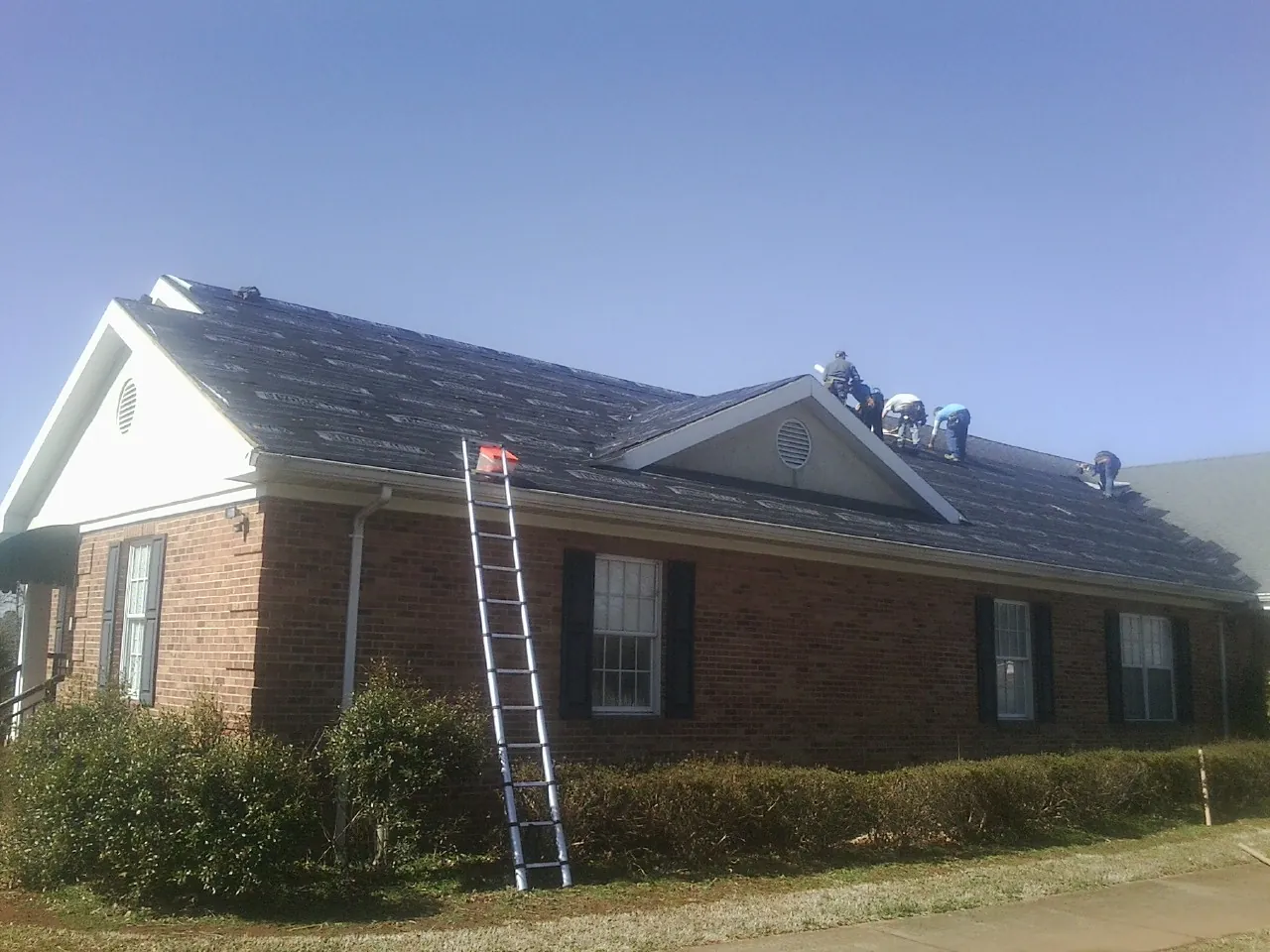 Crew tearing shingles off a brick ranch roof with a ladder set — Metal Roof Repair work by our crew in Martinsdale