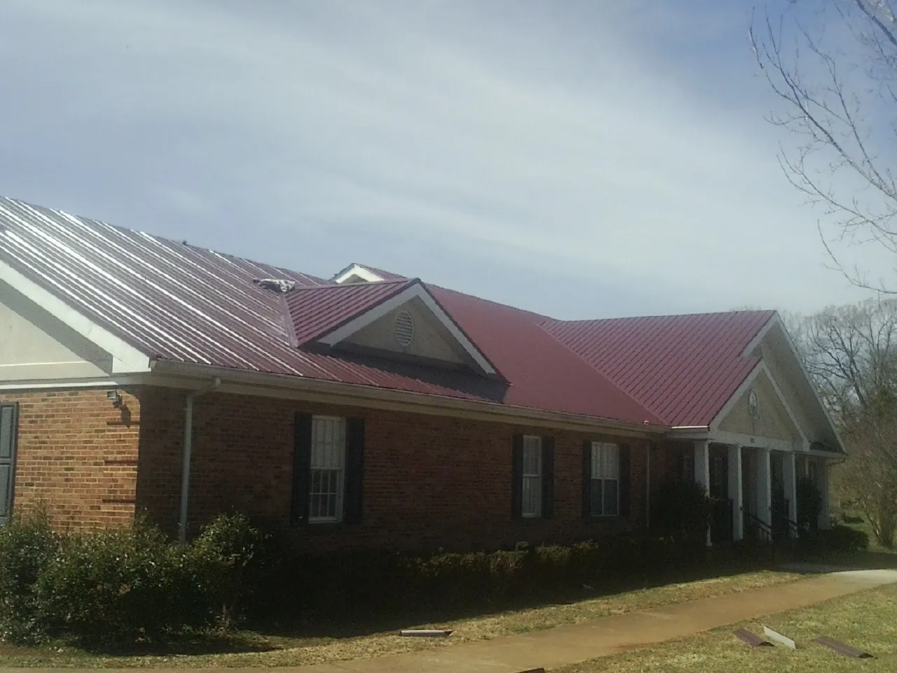 Red metal roof with gabled entries on a long brick building, from a Hail Damage Roof Repair job in Martinsdale