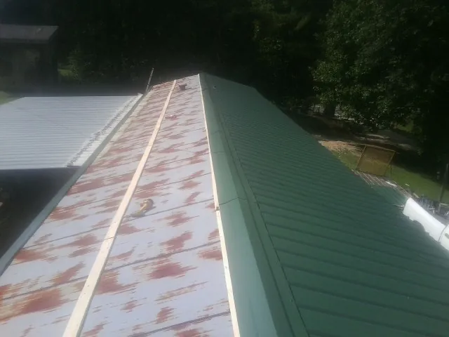 Old rusted panels beside newly installed green metal roofing — Wind Damage Roof Repair by Roofing Brothers in Martinsdale