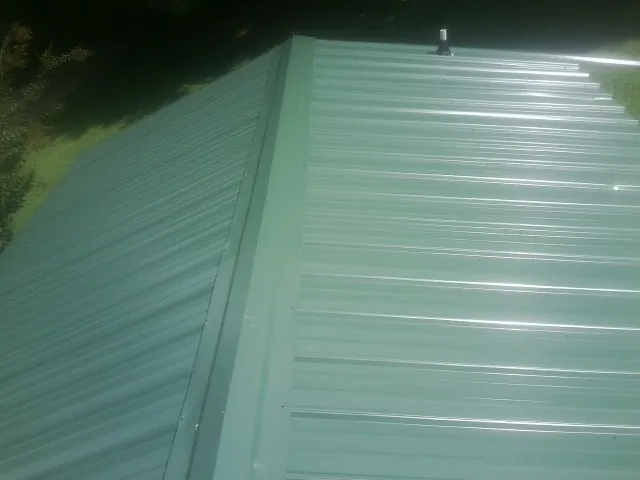 New green metal panels meeting at the ridge of a roof — Flat Roof Repair work by our crew in Martinsdale