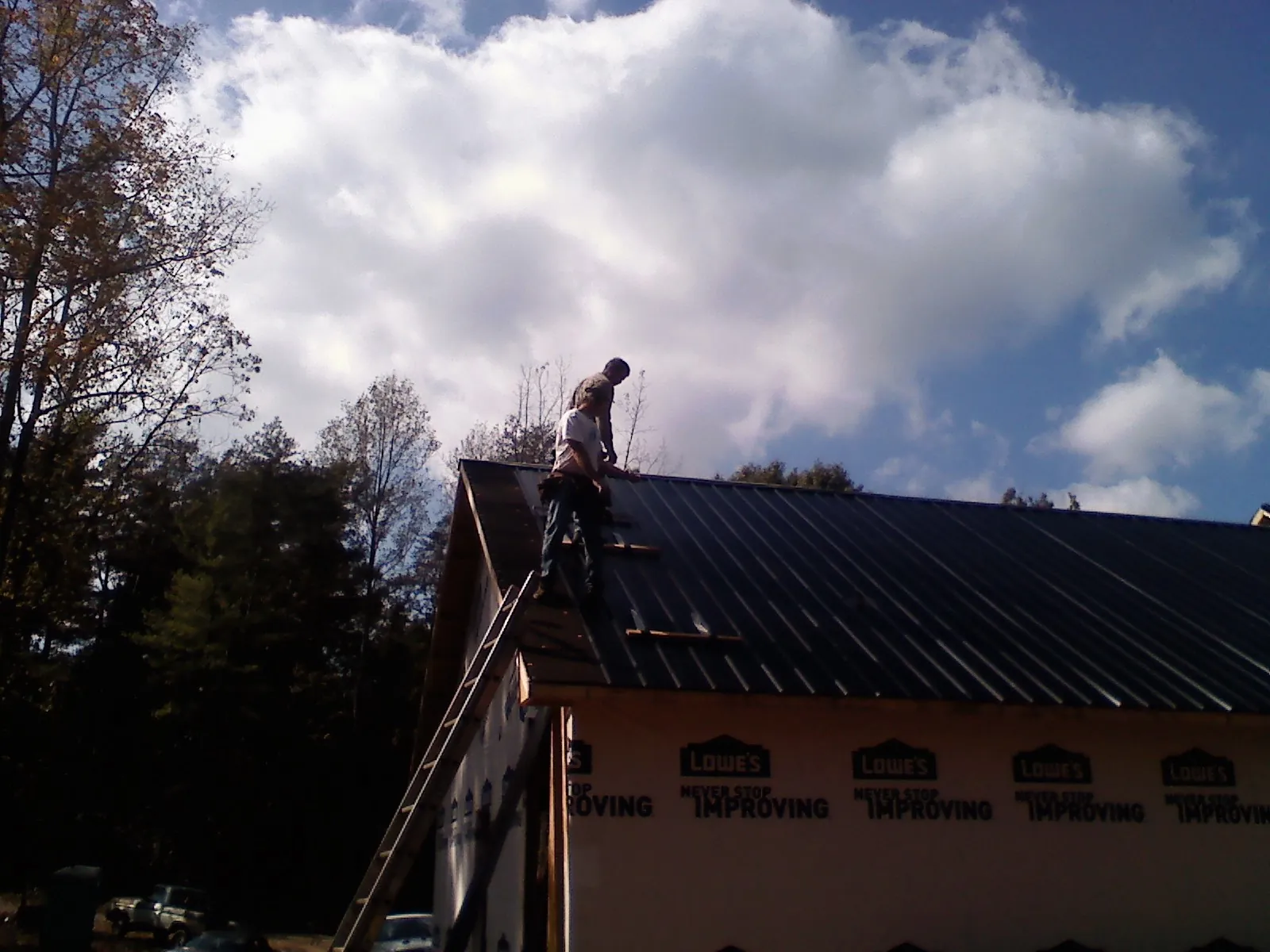 Roofer fastening dark metal panels high against a cloudy sky, from a Roof Inspection job in Martinsdale