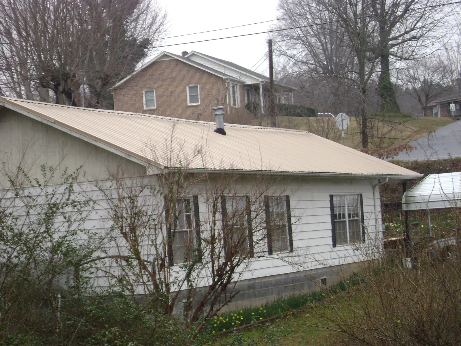 Tan metal roof on a white sided house set into a hillside — Commercial Roofing by Roofing Brothers in Martinsdale