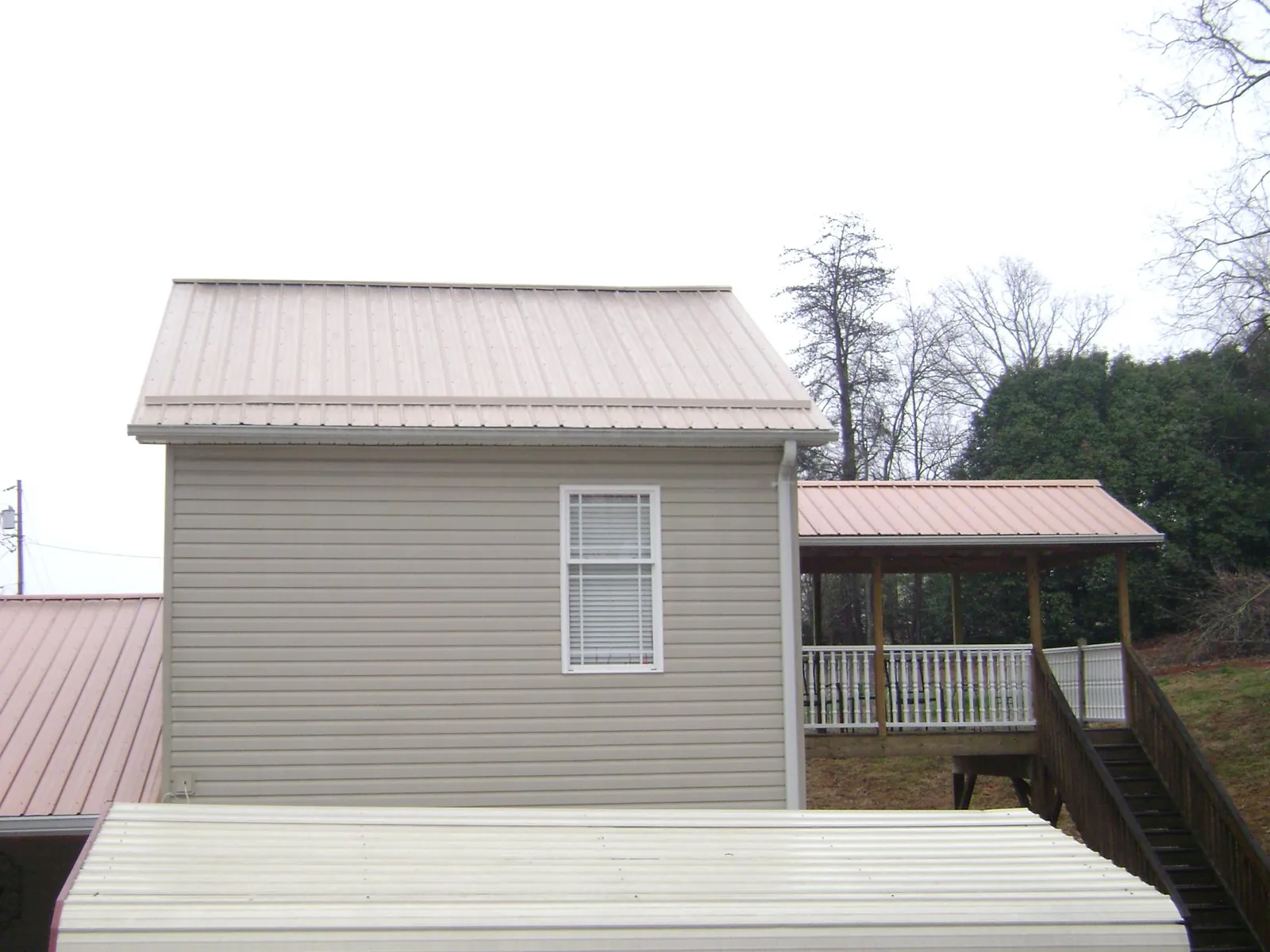 Tan metal roofs on a two story addition and attached porch, from a Roof Replacement job in Martinsdale